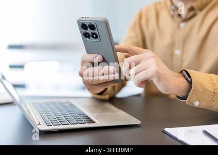 Digital communication and remote work, person using smartphone and laptop for business productivity in office. Professional multitasking with mobile technology and computer for efficient workflow. Stock Photo
