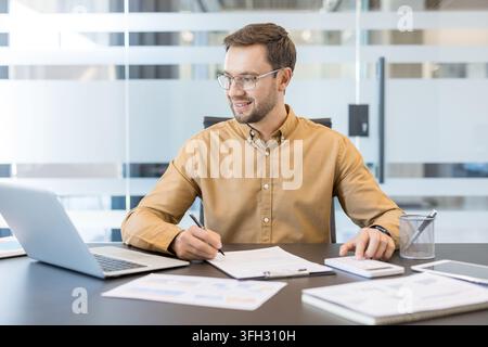 Financial planning and business analysis, professional man working with laptop and calculator in modern office. Corporate employee reviewing data and managing budget strategy. Stock Photo