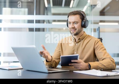 Remote work and virtual meeting, professional man using laptop and headphones for video conference in modern office. Business communication and digital collaboration, employee participating in online. Stock Photo