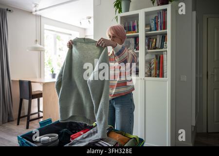Woman checking clothes for holiday trip before packing things in suitcase at home in bedroom. Stock Photo
