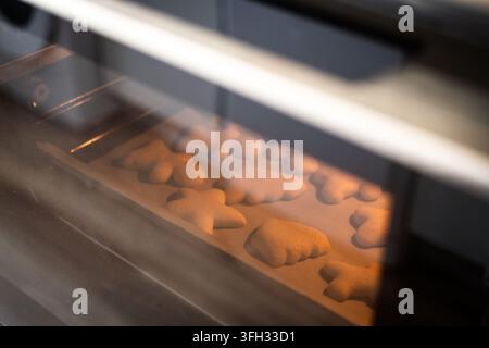 Christmas cookies in festive shapes baking on a tray inside a warm oven, viewed through the oven door. Stock Photo
