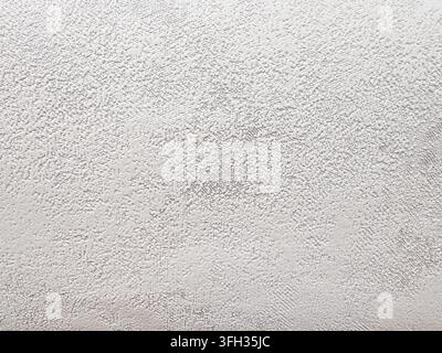 White painted wall presenting a rough stucco texture, forming an abstract and grainy pattern ideal for backgrounds, surfaces, or decorative design ele Stock Photo