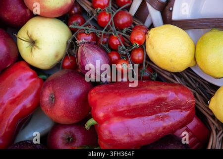 Fresh assorted fruits and vegetables arranged in wicker basket with apples, tomatoes, lemons, peppers, onion, close-up market produce display, with Stock Photo