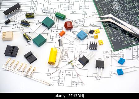Various electronic components scatter on a circuit diagram and a printed circuit board. Tools rest close by for assembly work. Stock Photo