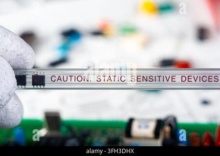 A person holds a caution sign about static sensitive devices while working with electronic components on a table filled with tools and parts. Stock Photo
