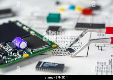 A person uses tweezers to place an electronic part on a circuit board in a workshop. Tools and parts are scattered around. Stock Photo