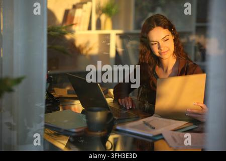 Telecommuter checking documents working at home viewed through a window Stock Photo