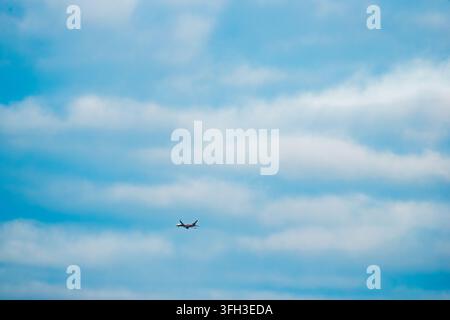A passenger airplane flying through soft white clouds across a bright blue sky Stock Photo