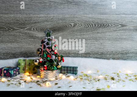 Small festive christmas tree decorating snowy scene with wrapped gifts and twinkling lights Stock Photo