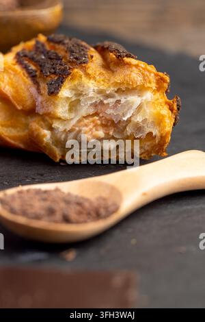 Piece of baked marble cake with tasty cream inside, fresh cut marble cake dessert is presented alongside ground cocoa particles on dark kitchen tablet Stock Photo