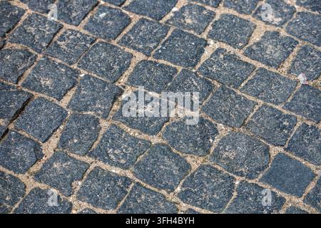 High angle view of a dark granite cobblestone pavement texture with sandy filler between stones. The uniform paving pattern presents a durable traditi Stock Photo