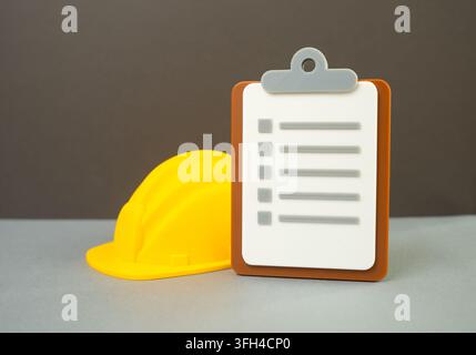 A yellow hard hat and a paper tablet. Safety inspection. Concept of workplace safety standards and quality control. Construction site checks and audit Stock Photo