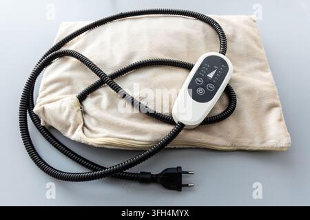A beige electric heating pad with a controller on a grey background Stock Photo