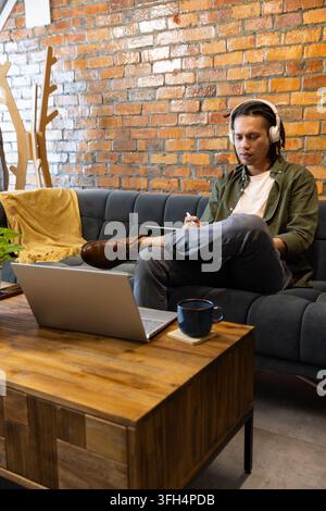 African American man sitting on sofa in cafe with headphones taking notes using laptop, copy space Stock Photo