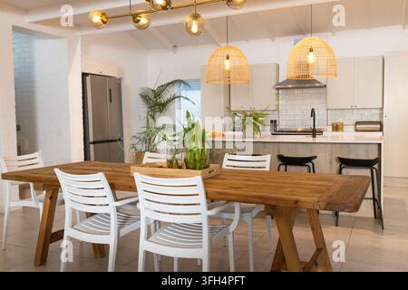 Wooden farmhouse dining table is anchoring open-plan kitchen and dining area, with potted plants Stock Photo