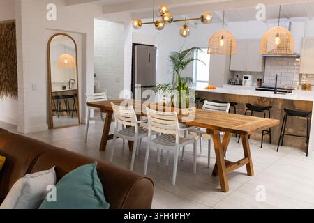 Long wooden trestle dining table is anchoring open-plan dining area with planter, gold chandelier Stock Photo