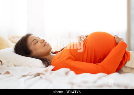 Pregnant Black woman lies comfortably on bed at home with eyes closed Stock Photo