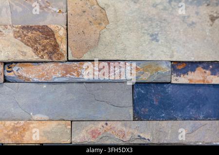 Close-up of a rustic exterior stone wall made of stacked multicolored slate and natural rock tiles with diverse textures. Stock Photo