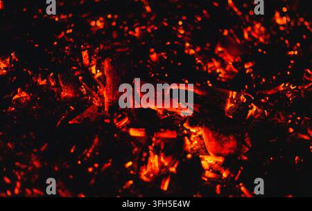 Close-up of glowing hot embers and burning wood in a campfire at night, radiating intense red heat and warm cozy light. Stock Photo