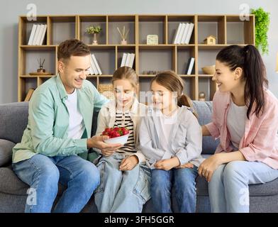 Happy family with two daughters eating strawberries together on couch at home Stock Photo