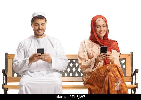 Middle eastern man and woman in ethnic clothes sitting on a bench and using smartphones isolated on white background Stock Photo
