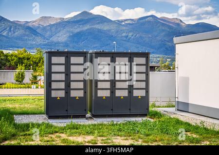 Industrial electrical transformer cabinets standing in a field against a mountain landscape Stock Photo