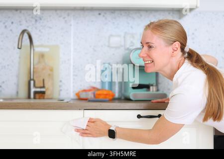 Woman cleaning cabinet doors in a modern kitchen, ideal for advertising household products and professional cleaning services. Stock Photo