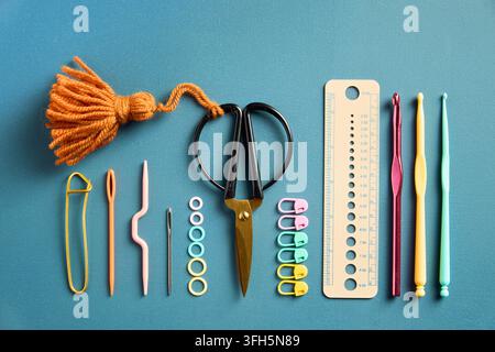 A collection of colorful knitting and crochet tools neatly arranged on a blue background, with yarn, needles, hooks, scissors and accessories for crea Stock Photo