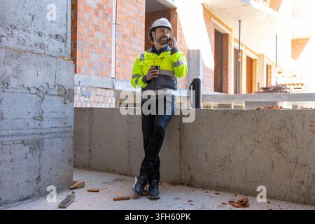 Male engineer talking on smartphone and holding cup Stock Photo