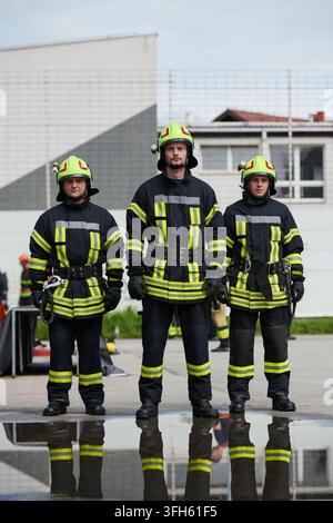 Three Firefighters Standing Together in Protective Gear With Helmets and Puddle Reflection Stock Photo