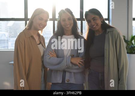 Diverse female coworkers standing together posing by office window with cardigan and lens flare Stock Photo