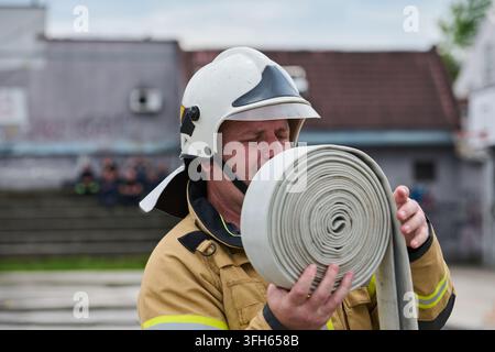 Firefighter Preparing Rolled Fire Hose While Wearing Helmet And Protective Turnout Gear During Training Stock Photo