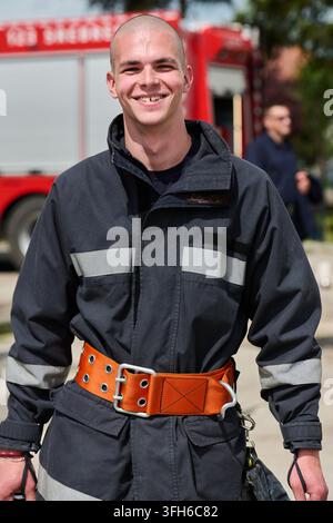 Smiling Firefighter in Protective Gear With Bright Safety Belt Standing by Fire Truck Stock Photo