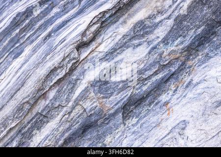Close-up of weathered stone surface with gray, white, and brown mineral veins. Textured rock shows natural erosion patterns and rough, layered appeara Stock Photo