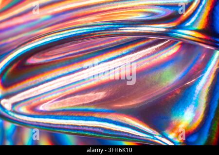 Abstract close-up of an iridescent holographic metal surface, featuring vivid rainbow reflections, flowing curved lines, and luminous chromatic textur Stock Photo