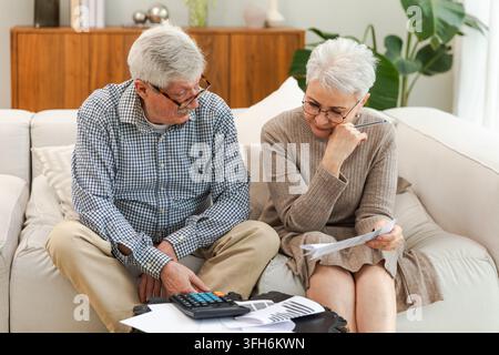 Middle aged senior couple sit with laptop and paper document. Older mature man woman reading paper bill pay online at home managing bank finances calculating taxes planning loan debt pension payment Stock Photo