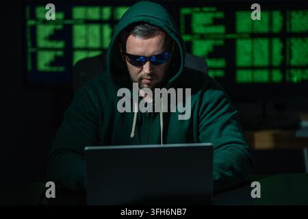 Hacker uses laptop for hacking activity. Hacker analyzes encryption and firewall system. Hacker monitors digital data flow. Hacker attempts identity Stock Photo