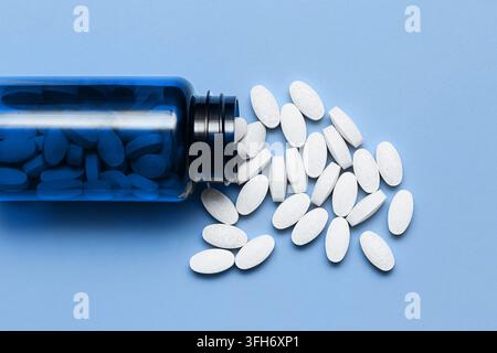 White supplement tablets beside open blue bottle on light surface. Health background for vitamins medication pharmacy wellness and daily supplement. Stock Photo