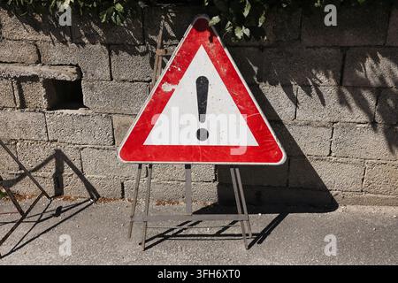 Red triangular warning sign with exclamation mark beside brick wall. Safety background for danger caution hazard attention and public information. Stock Photo