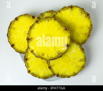 Top view of several bright yellow juicy pineapple slices arranged on a transparent plate against white background. Ideal for healthy eating, tropical Stock Photo