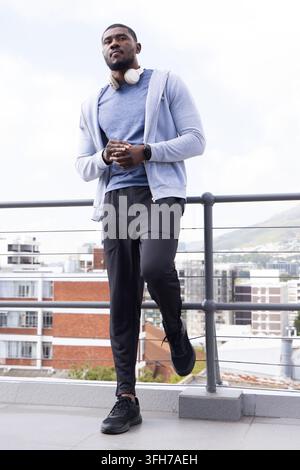 Man standing on rooftop terrace leaning on railing with headphones and smartwatch Stock Photo