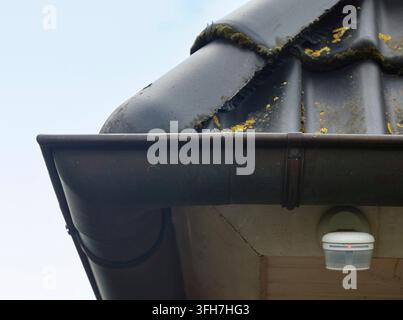 Motion sensor with a red light mounted under a house gutter and roof tiles Stock Photo