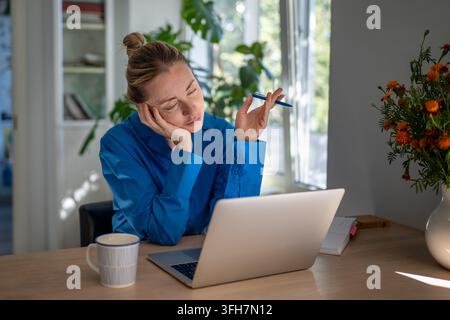 Tired bored woman remote worker exhausted and getting sleepy while working on laptop at home office. Stock Photo