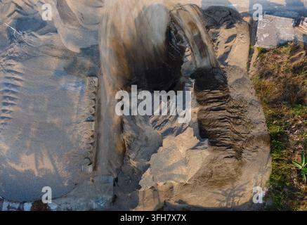 Aerial view of a sand mining site with large piles of excavated earth and sand, showing textured ground patterns and tracks in Cilongok, Central Java, Stock Photo