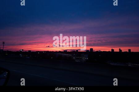 Dramatic pink and red sunset sky over a dark urban skyline at dusk. Vivid pink, red and purple sunset clouds glowing above a dark urban skyline Stock Photo