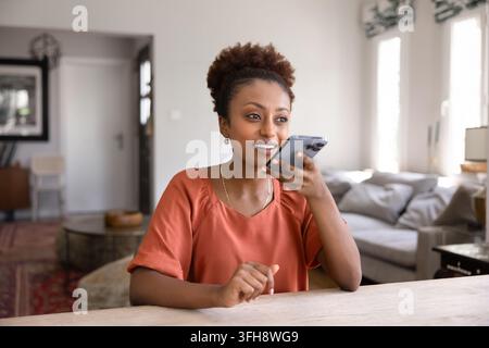 Young 25s African woman using voice assistant on smartphone Stock Photo