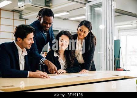In a meeting room, a diverse international team, led by a female boss, engages in lively discussion. Together, they review documents, analyze graphs, Stock Photo