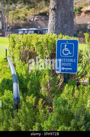 Blue accessible route sign with wheelchair symbol and directional arrow in a landscaped outdoor area on Santa Catalina Island, California, USA. Stock Photo
