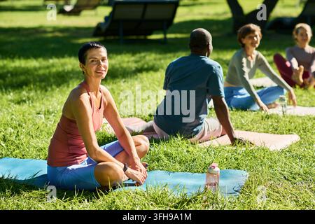 Portrait of Mature Woman Practicing Outdoor Yoga with Group in Park Stock Photo