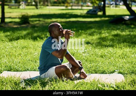 Middle Aged Black Man Drinking Water on Mat in Park Stock Photo